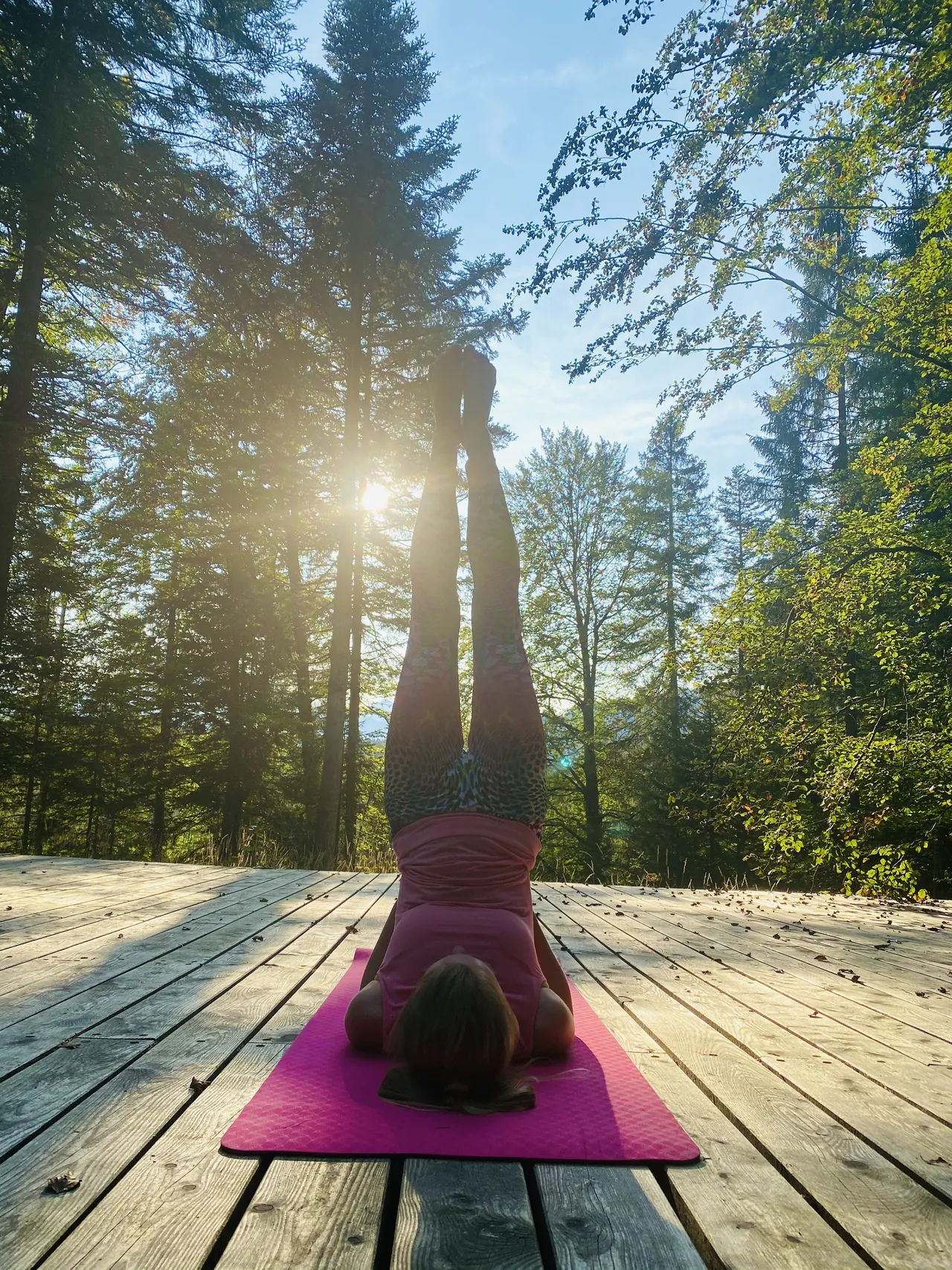 Adina übt einen Schulterstand auf einer pinken Yogamatte im sonnigen Wald.