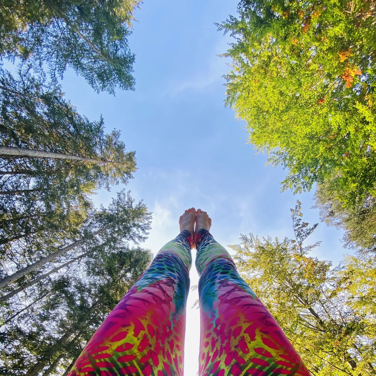 Barfüße über bunt gemusterten Yogaleggings vor blauem Himmel und grünen Baumkronen.