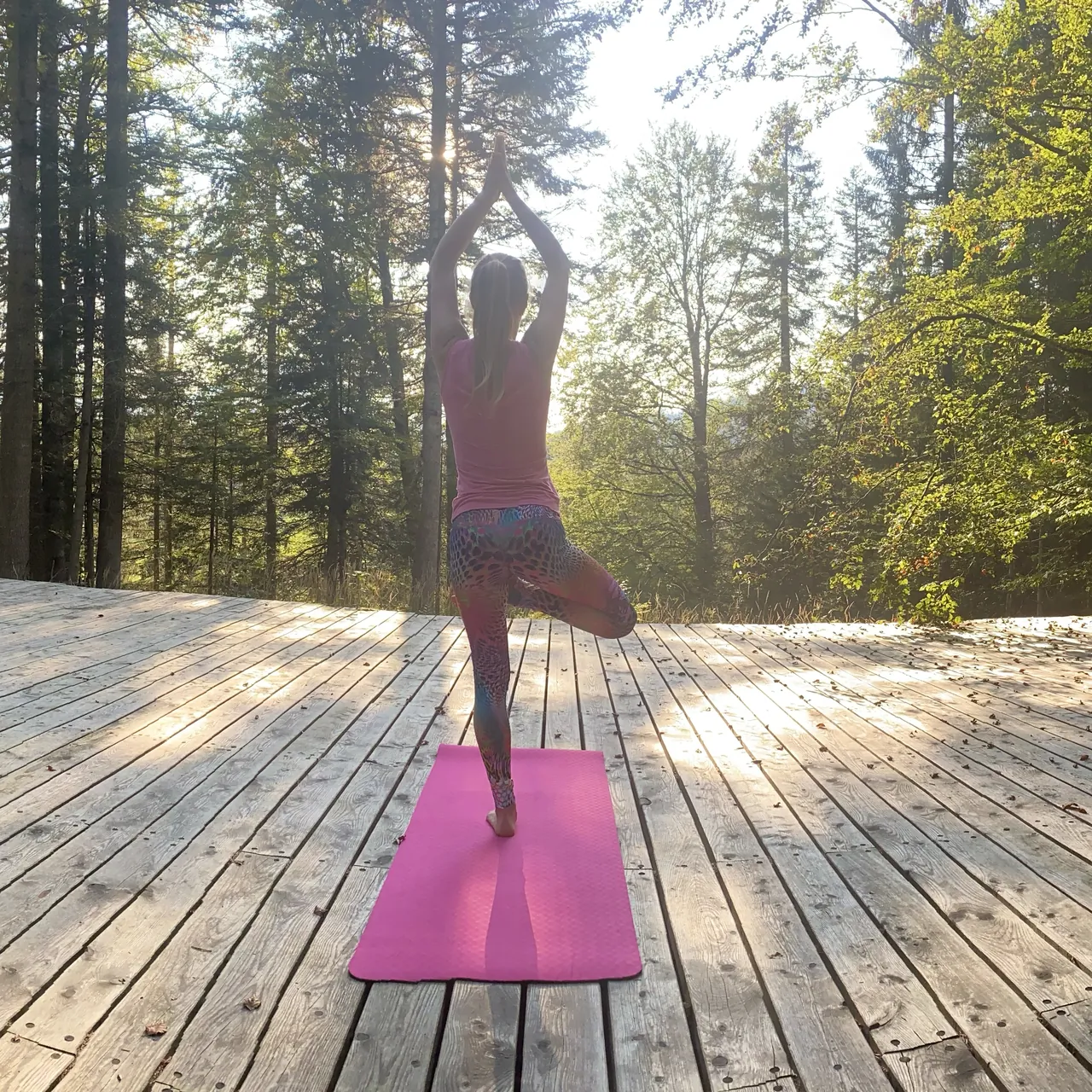 Adina übt den Baum auf einer weitläufigen Holzterrasse im Wald.