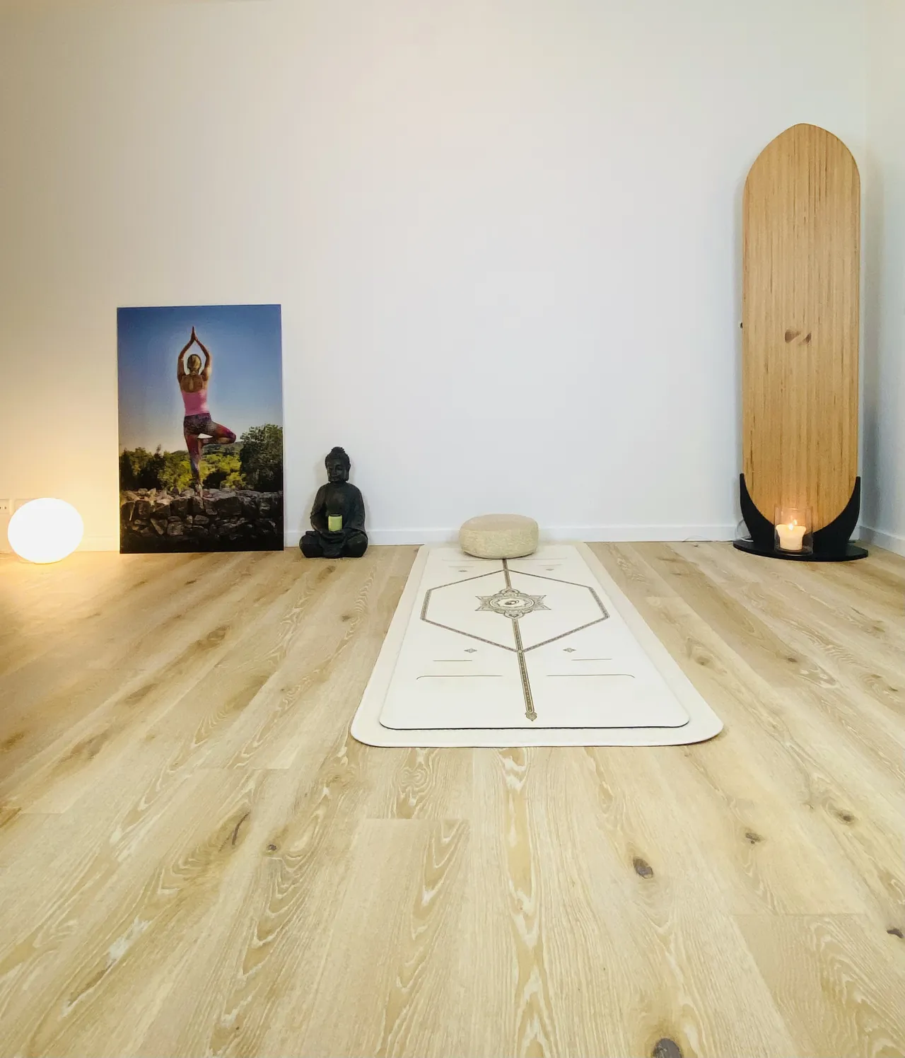 Heller, ruhiger Yogaraum mit Yogamatte, Sitzkissen, Buddhafigur und warmem Licht.